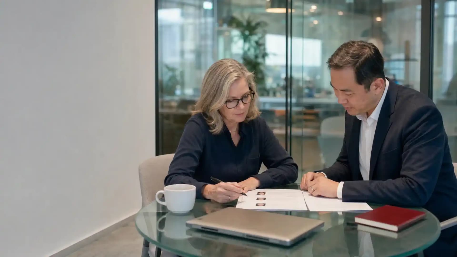 A recruiter and hiring manager review a short candidate shortlist together at a glass table